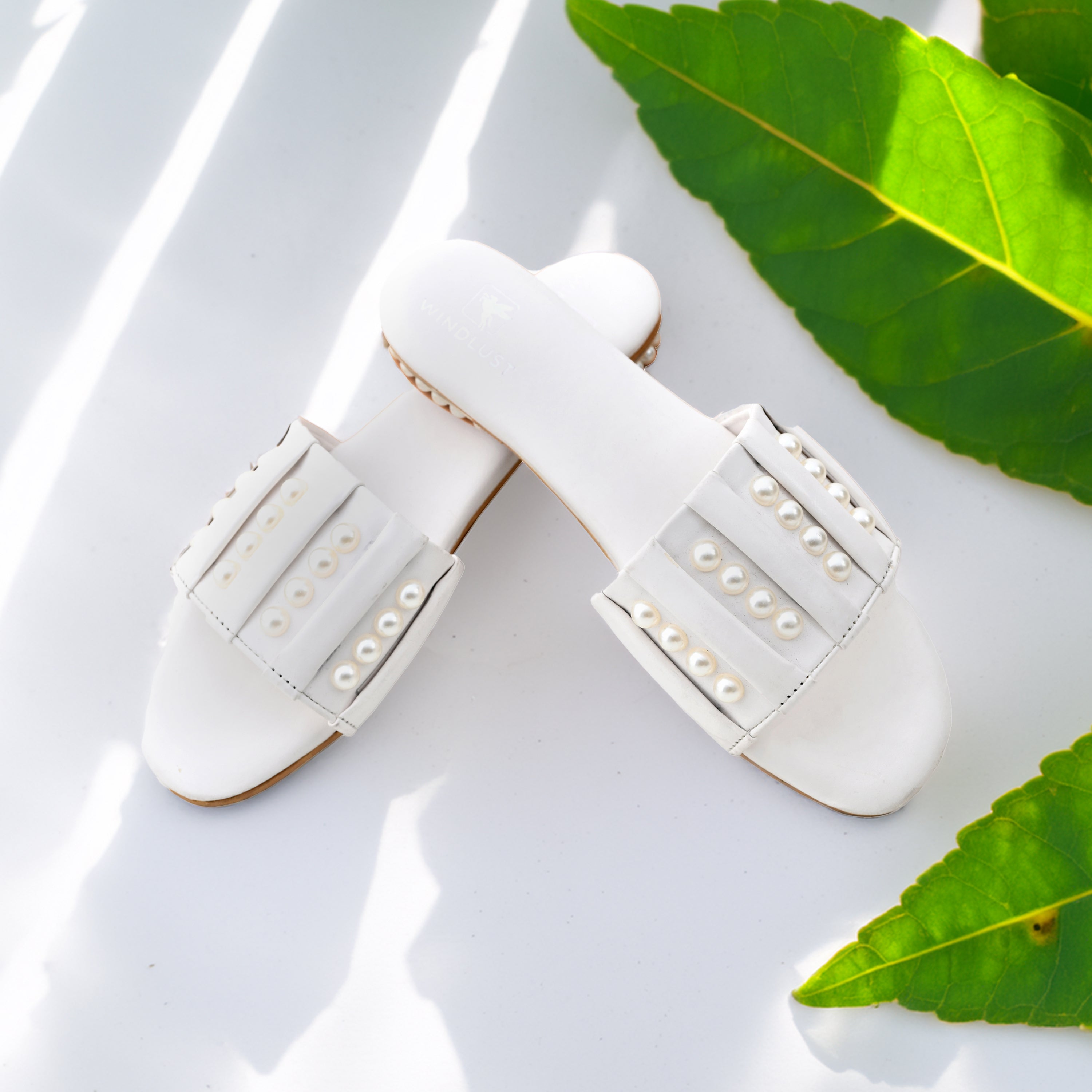 White linear pearl flats by Windlust showing elegant slip-on design with pearl embellishments on smooth white fabric.